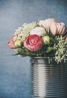 Bouquet of white and pink flowers with green foliage inside a decorative tin.